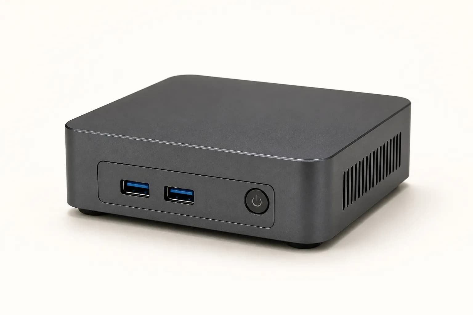 Small square dark-grey mini PC standing on a desk beside a cable.
